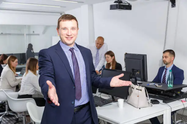 Photo of Positive businessman standing in coworking space with open hand