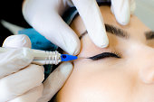 Cosmetologist applying permanent make up eyeliner, eyeliner tattoo procedure