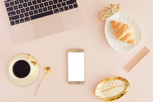 Feminine office workplace with mobile phone, coffee and croissant. Mockup with laptop. Flat lay for social media blogger