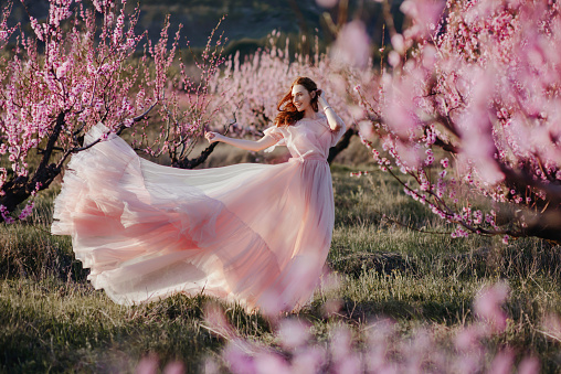 Beautiful young girl under the flowering pink spring tree