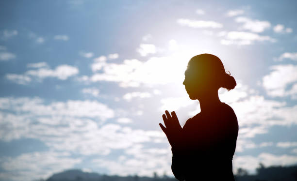 istock silhouette of female practicing yoga by basic posture with daylight and blue sky, White clouds, Healthcare concept. 1130659906