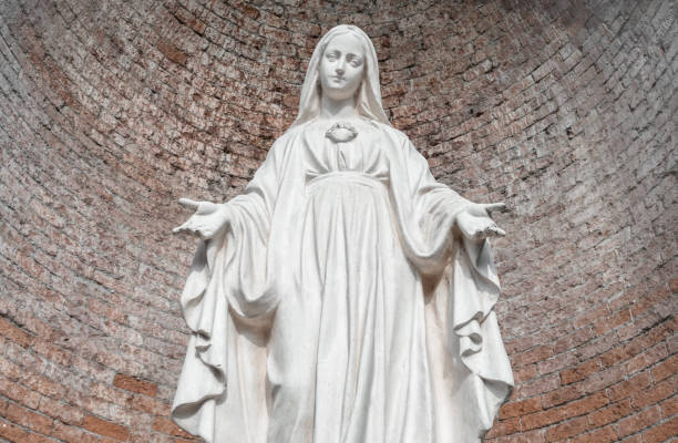 Statue in stone of Virgin Mary. On background, red brick wall. Ideal for christmas and easter concepts and other.