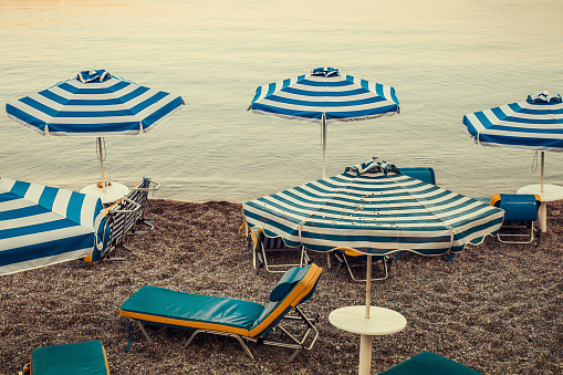 Striped beach umbrellas and sunbeds by the sea in Haraki, Greece