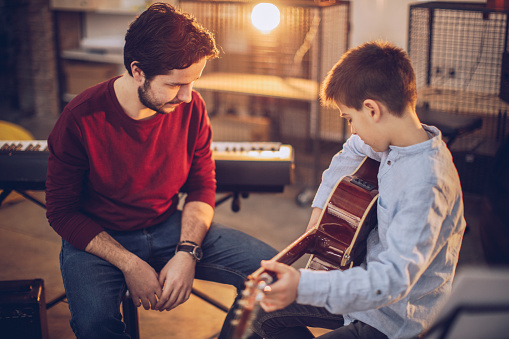 Two people, man guitar teacher working with little boy on guitar lessons.