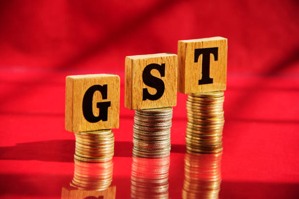 Wooden letters GST and money coin stack on red table background, financial concept stock photo