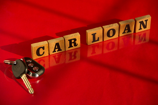 Wooden letters CAR LOAN with car key on a red background, financial concept