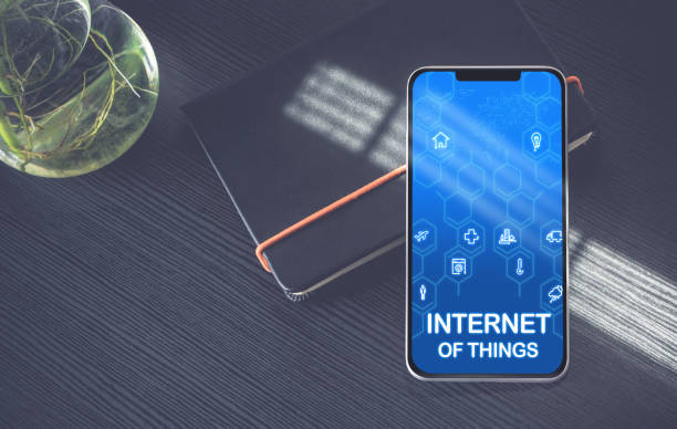 istock Internet of things (IoT) features icons on mobile phone screen lay on black notebook near window with sunlight on black wooden desk,Digital age technology concept. 1130670323