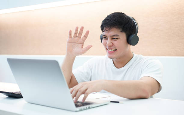 close up young asian student man wearing headset and greeting on video conference with friends or family in relax time , technology lifestyle concept - video conference imagens e fotografias de stock
