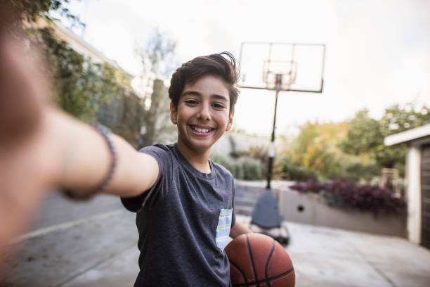 ヒスパニックの若い男の子は自分撮りを取り、彼の手にバスケットボールを保持しています - 一人称目線 ストックフォトと画像