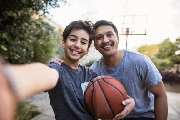 padre e hijo hispanos tomando un selfie al aire libre mientras juegan al baloncesto - bouncing ball family playing fotografías e imágenes de stock