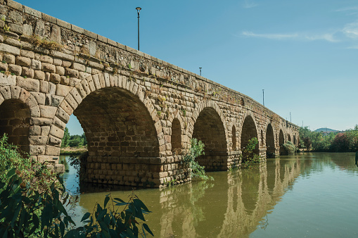Stone arches of the Puente Romano, an ancient long bridge over the calm Guadiana River at Merida. Founded by ancient Rome in western Spain, the city preserves many buildings of that era.