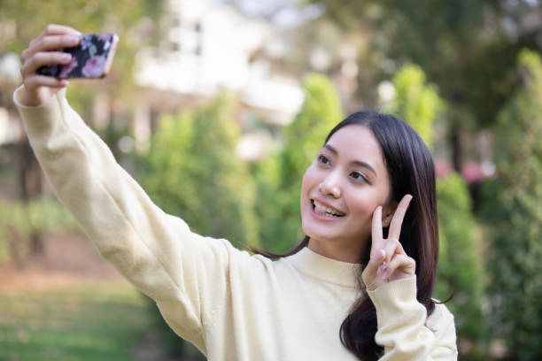 istock Woman Gesturing Peace Sign While Taking Selfie Against Trees 1130692523