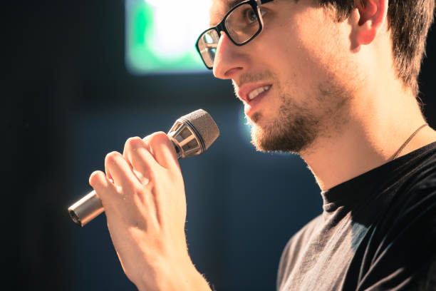 istock Speaker on the stage: Young Caucasian man is talking into a mirophone 1130693099