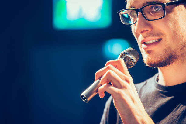 istock Speaker on the stage: Young Caucasian man is talking into a mirophone 1130693129