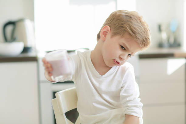 テーブルで食べる子供やブロンドの幸せな男の子。子供時代と幸福、独立。朝食、朝、家族。小さな男の子はバナナを食べて牛乳を飲む。健康的な食事とビタミン。ダイエット, ベジタリア� - eating cereal student human mouth ストックフォトと画像