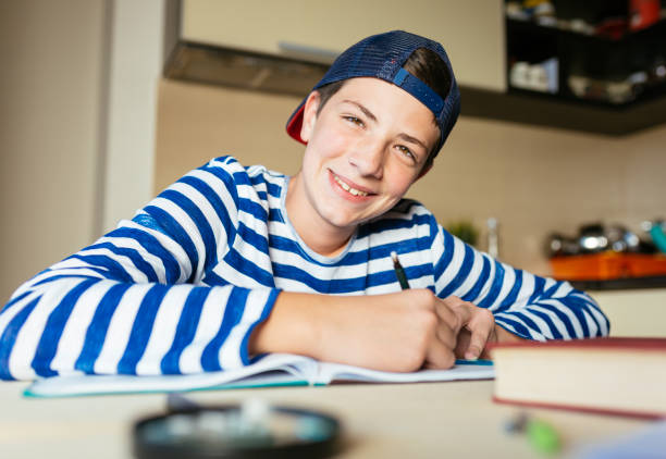 Schoolboy doing homework at living room Photo of teenage boy doing homework at home boring homework twelve stock pictures, royalty-free photos & images