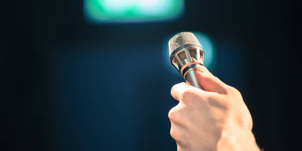 Speaker on the stage: Young Caucasian man is talking into a mirophone Young man on the stage is talking into a microphone, speech interview seminar microphone inside of stock pictures, royalty-free photos & images