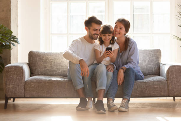 glückliche familie und kind, die spaß mit smartphone zu hause haben - parent playful father mother stock-fotos und bilder