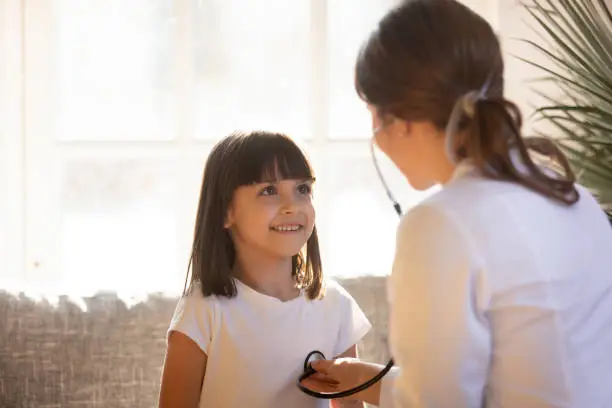 Photo of Cute kid visiting female doctor pediatrician holding stethoscope examining child