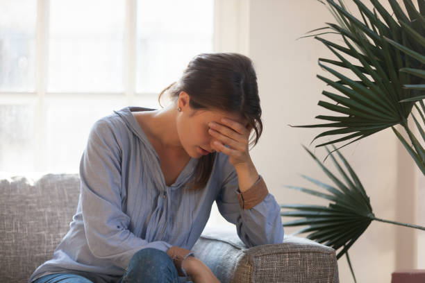 malestar deprimido mujer sensación cansado tener dolor de cabeza sentado en el sofá - mental abuse fotografías e imágenes de stock