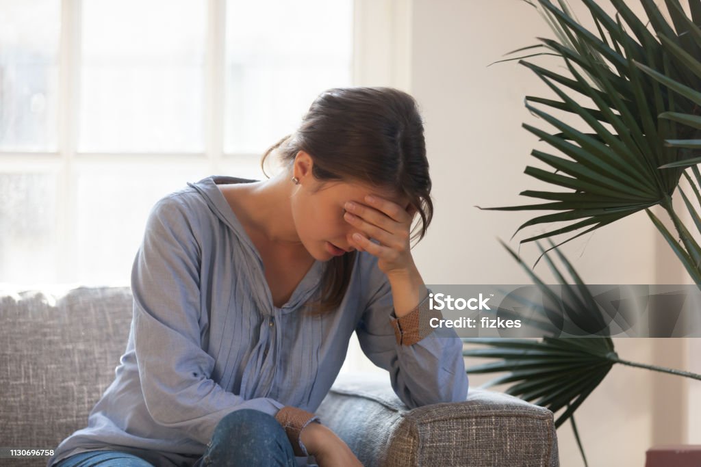 Upset depressed woman feeling tired having headache sitting on couch Upset depressed young woman feeling tired bad down headache migraine sitting on couch, sad desperate ashamed female in trouble having problem, regret mistake abortion, crying alone at home Women Stock Photo