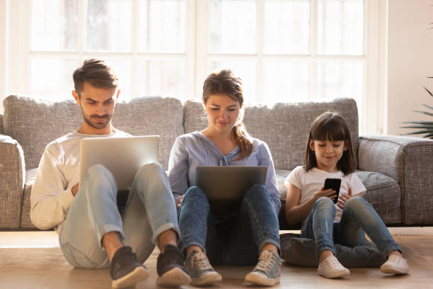 istock Family with kid sitting on floor at home using devices 1130696772