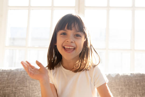 Happy cute little youtuber vlogger waving hand looking at camera Happy cute little youtuber vlogger waving hand saying hello hi looking at camera talking to webcam, smiling kid child girl making online video call recording vlog sitting on sofa at home, portrait one girl only stock pictures, royalty-free photos & images