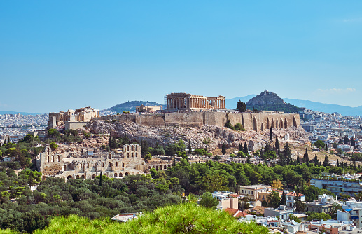 View of Athens, Greece, under the brilliance of a sunny summer day, with the iconic Mount Lycabettus towering over downtown. From this vantage point, the city sprawls out beneath the hill, showcasing a blend of ancient and modern architecture. Lycabettus Hill stands as a timeless sentinel, offering a stunning backdrop to the vibrant urban landscape. As the sunlight bathes the scene in warmth, immerse yourself in the beauty of Athens and the commanding presence of Mount Lycabettus, capturing the essence of a perfect summer day in the Greek capital.