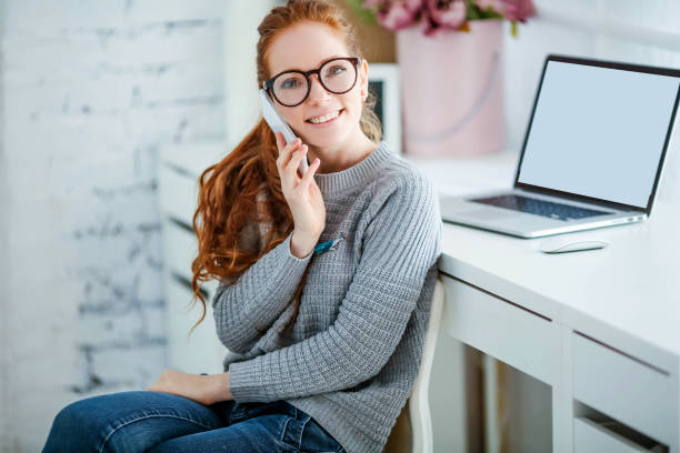 menina bem sucedida que trabalha no escritório. ela tem cabelo ruivo e um belo sorriso no rosto - business mobile phone telephone women - fotografias e filmes do acervo