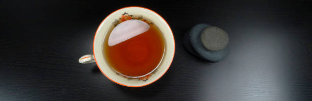 heißen tee tasse porselain mit entspannenden steinen auf einem schwarzen hintergrund aus holz - jasmine tea black tea tea drink stock-fotos und bilder