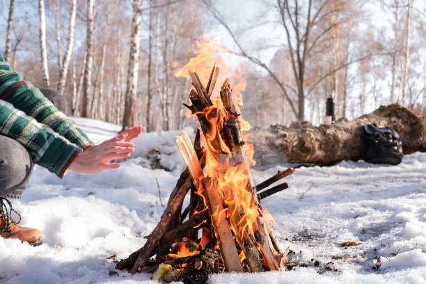 Female person near a fire on a sunny winter day in the woods