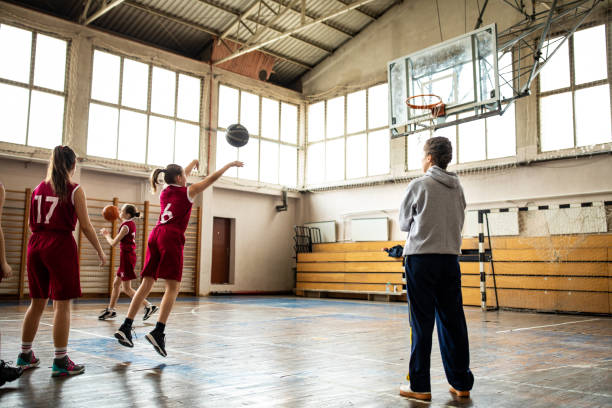 Female coach watching teenage girls practicing free throws