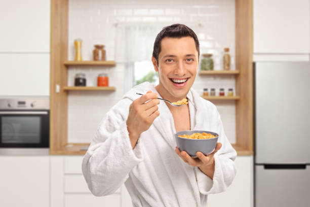 istock Smiling young man in a dressing gown eating cereal from a bowl in a kitchen 1130721192