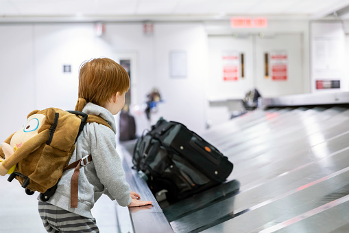 Child Traveler Waiting for Suitcase on Conveyor Belt in Airport