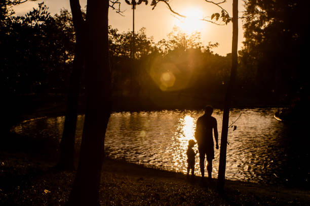 ojciec i syn bawią się w parku w pobliżu jeziora o zachodzie słońca.  koncepcja rodzinnej miłości i fotografii sylwetki wakacji - mother superior zdjęcia i obrazy z banku zdjęć