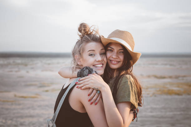 Portrait of smiling young women embracing in desert. Multi-ethnic female friends are standing against sky. They are enjoying vacation together.