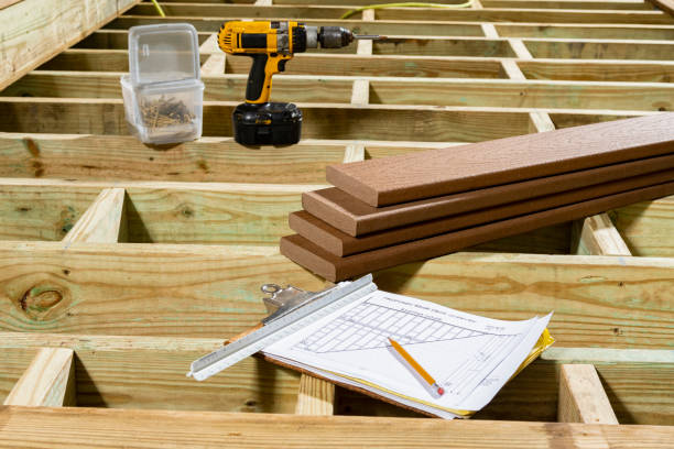 A clipboard with the deck design, pencil and sitting on joist framed with pressure treated southern yellow pine lumber with a stack of composite decking boards and screw gun in the background. In most parts of the country plans have to be submitted to the local government for approval before construction can begin.