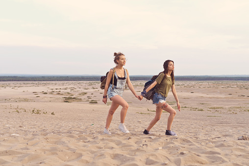 Young women holding hands while walking on sand. Female friends are hiking in desert. They are spending vacation together.