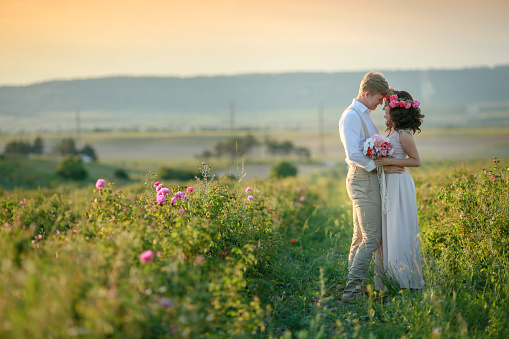 Happy young couple man and woman, adult romantic family. Meet the sunset in a wheat field. Happy smiling. The girl in her hands holds a gift, a bouquet of flowers, from roses