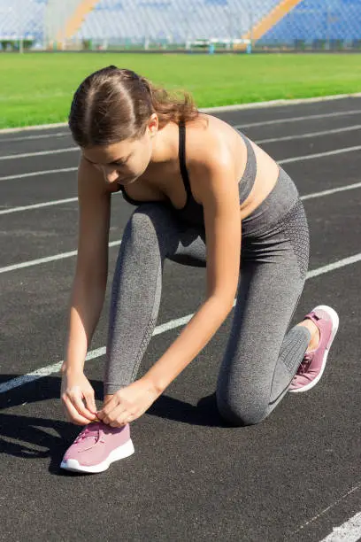 young sportsgirl tying her shoelaces on run track in Sport area, sport and fitness concept.