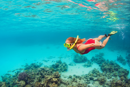 Young happy girl in snorkeling mask jump and dive underwater to see tropical fishes in coral reef sea pool. Travel activity, water sports, outdoor adventure, on family summer beach holiday with kids
