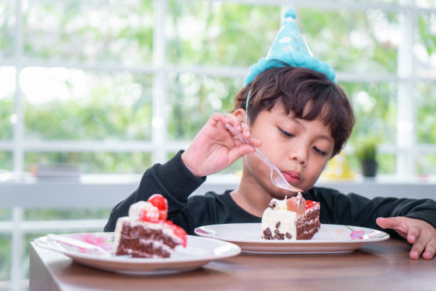 istock Asian Kid with party hat is eating birthday chocolate cake 1130748062