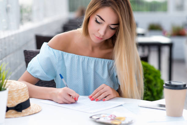 beau café d'été de fille. remplit l'écriture contractuelle, le contrat légal pour les services. rédaction d'un document certifié légalement correct. robe de cheveux longue femme. dame d'affaires travaillant véranda restaurant. - paper document pen long hair photos et images de collection