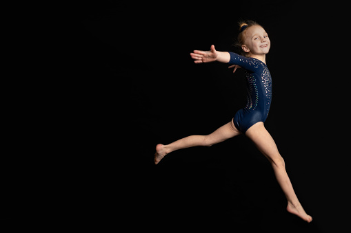 A beautiful 6 year old girl isolated on black leaping and smiling at the camera.