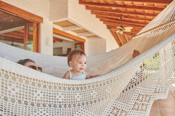 Playing baby girl with mom in hammock on vacation background