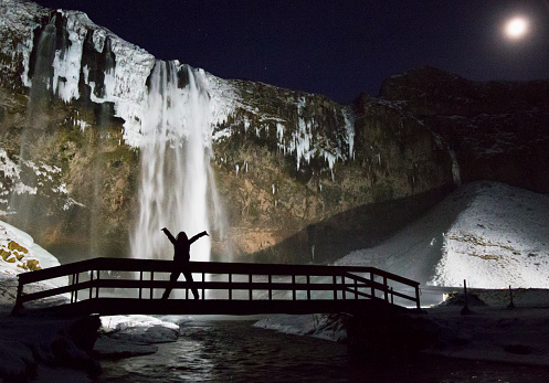 Seljalandsfoss waterfall night shot with unknown model on bridge over river on a winter night