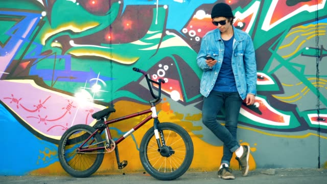Rider stands with a phone in hands. Young stylish Caucasian male teenager.