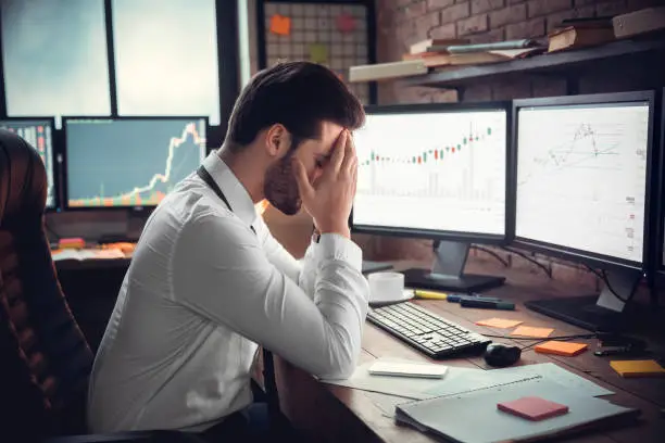 Frustrated depressed trader stressed by stock exchange fall on computer online graphs, sad desperate investor shocked by bankruptcy, financial crisis or money loss, tired businessman having headache