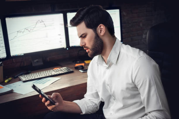 istock Young male trader at office work concept sitting holding smartphone confused 1130771119