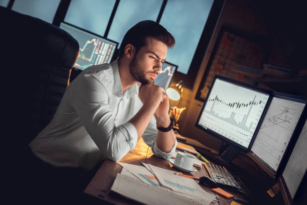 Focused thoughtful trader working at night analyzing stock trading graphs stock photo